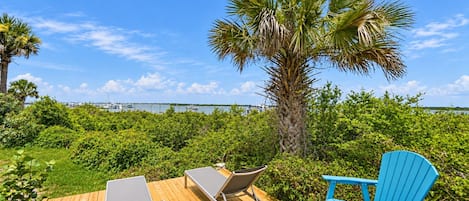 Um deck de madeira com duas cadeiras de sol e uma mesa, com vista para um porto e um corpo d'água.