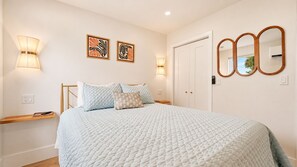 A bedroom with a bed, bedside lamps, a mirror, and artwork on the wall.