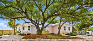 A two-story house with a large tree in front, a covered porch, and a small deck. - Pelican's Perch Cottage - New & Modern In Perfect Location w/ Waterfront Deck (St. Augustine)