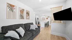 A modern living room with a grey sofa, decorative wall art, and a flat-screen TV mounted on a wooden wall. - Pelican's Perch Cottage - New & Modern In Perfect Location w/ Waterfront Deck (St. Augustine)