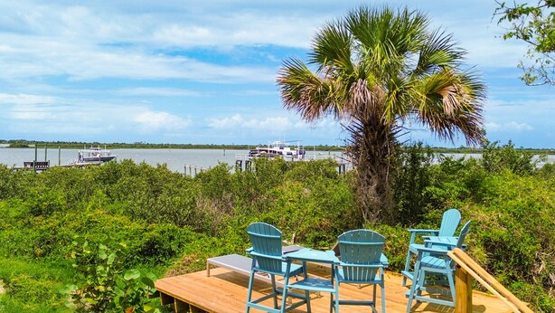 A wooden deck with chairs and a table overlooking a body of water with boats. - Pelican's Perch Cottage - New & Modern In Perfect Location w/ Waterfront Deck (St. Augustine)