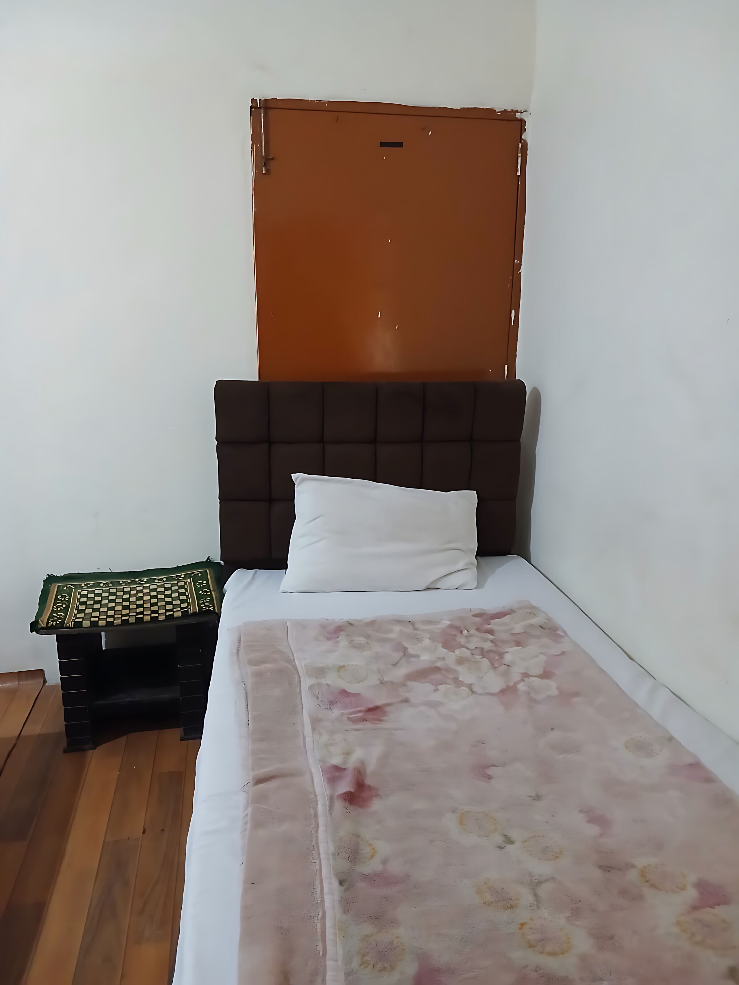 Een eenpersoonsbed met een bloemenprint sprei, een donker hoofdbord en een bruine deur.