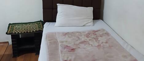 Una cama individual con colcha estampada, cabecera oscura y puerta marrón.