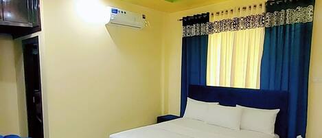 A hotel room with a bed, a ceiling fan, an air conditioning unit, a TV, and a blue armchair.