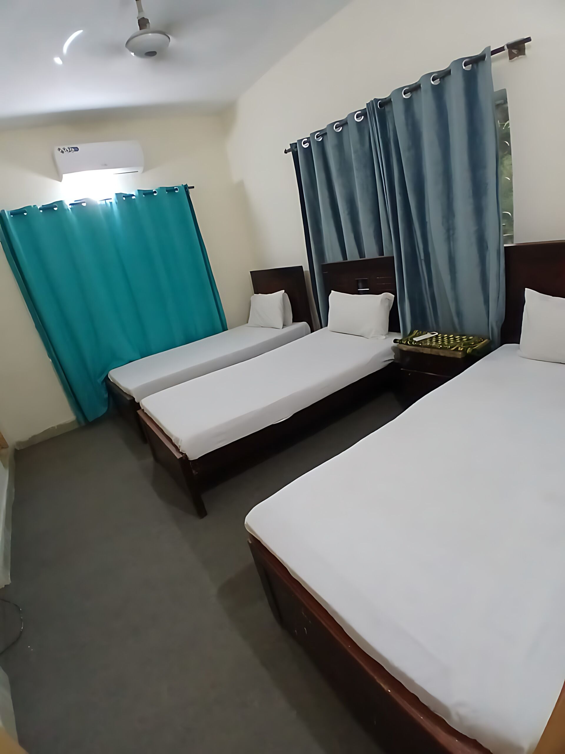 Une chambre d’hôtel avec deux lits simples, un ventilateur de plafond et une fenêtre avec des rideaux.
