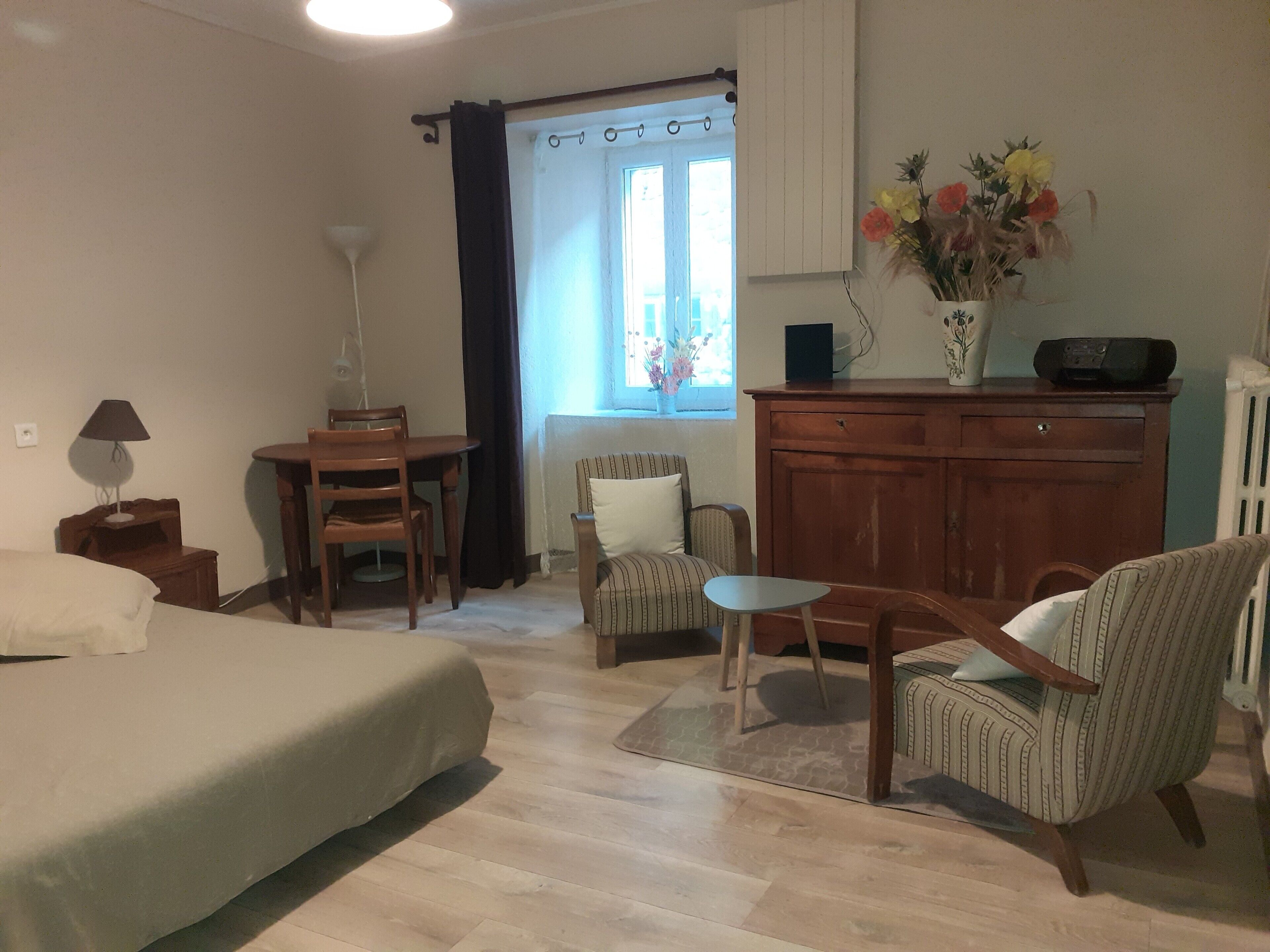 Una habitación con cama, escritorio, silla, mesita, armario y ventana con cortinas.