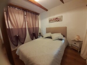 Ein Schlafzimmer mit einem Bett, einem Nachttisch, einer Lampe und durchsichtigen Vorhängen.