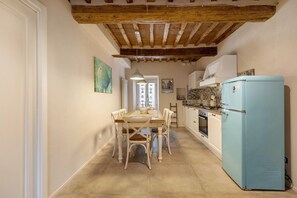 Una cocina con refrigerador azul, vigas de techo de madera, una mesa de comedor con sillas y una lámpara colgante.