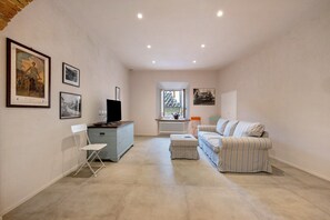 Una habitación amplia con sofá, televisión, una mesita y ventana.