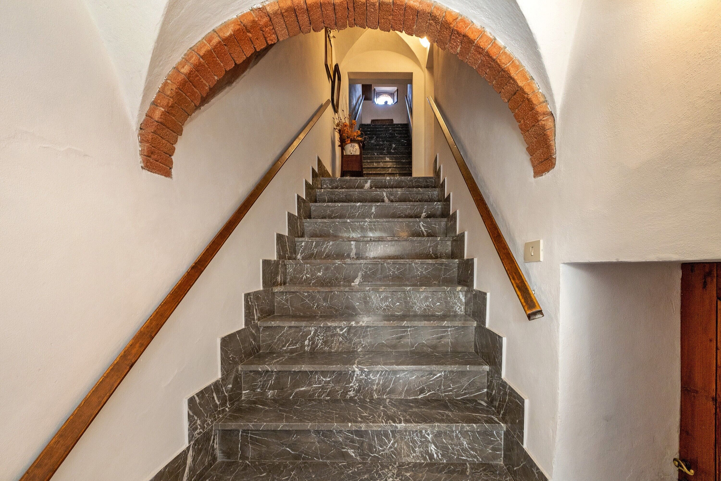Un escalier en marbre avec une rampe en bois et une arche en briques menant à une pièce comprenant un lit et une table de chevet.