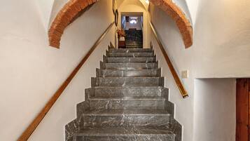 Un escalier en marbre avec une rampe en bois et une arche en briques menant à une pièce comprenant un lit et une table de chevet.