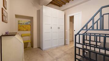 A hallway with a staircase, a white wardrobe, a yellow chair, and a painting on the wall.