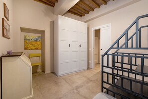 Un pasillo con una escalera, un armario blanco, una silla amarilla y un cuadro en la pared.