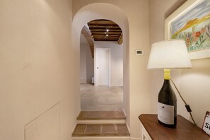 Un pasillo con una escalera que conduce a otra habitación, una lámpara sobre una mesa y una botella de vino.