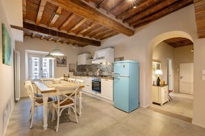 Una cocina con armarios blancos, un refrigerador azul y una zona de comedor con sillas blancas.