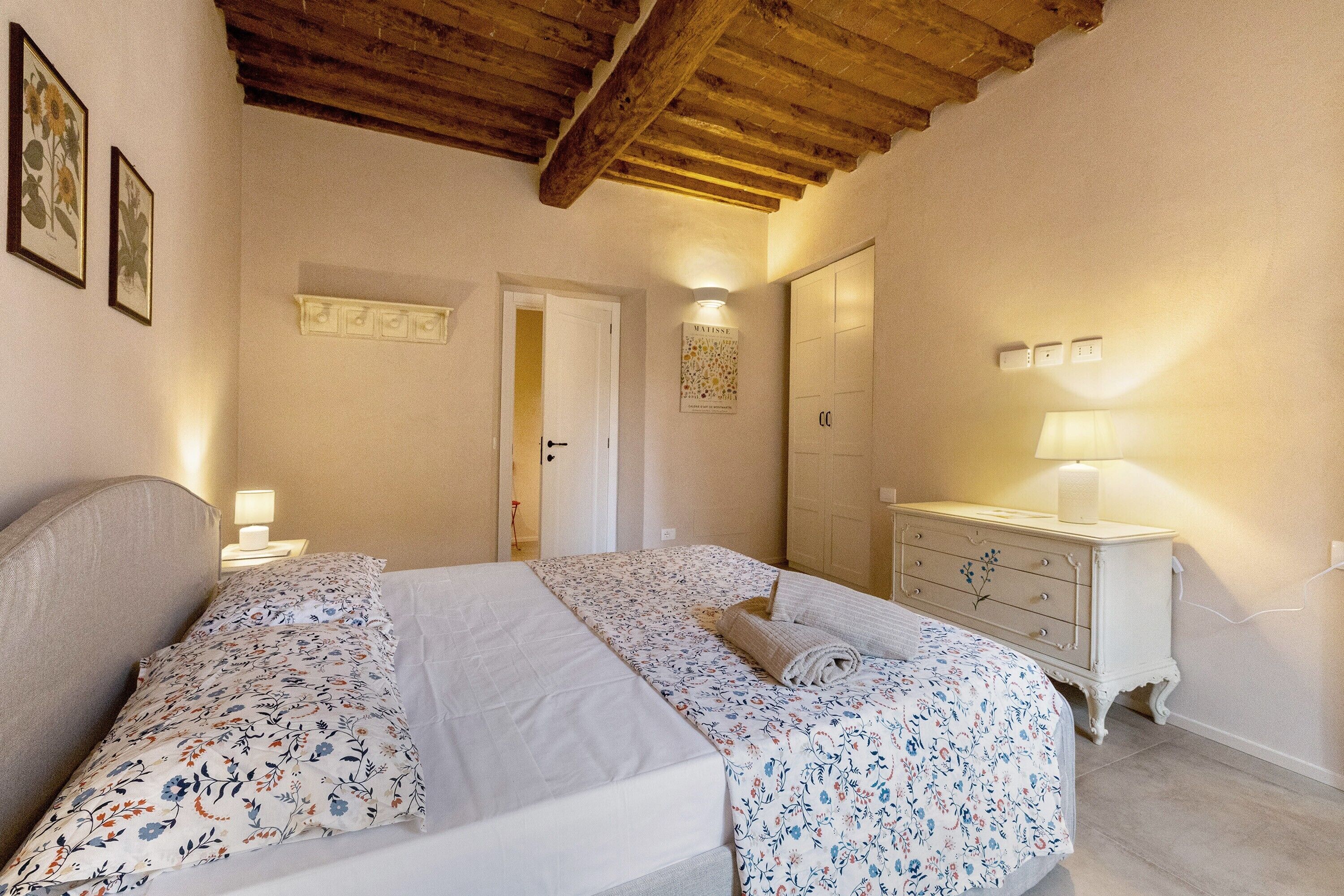 Une chambre à coucher avec un lit double, une commode, une table de chevet et une porte donnant sur une autre pièce.