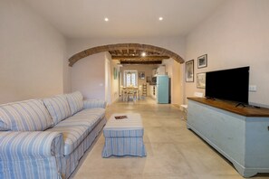 Una sala de estar con un sofá, un reposapiés y un televisor sobre un mueble.