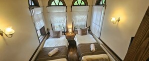 A narrow corridor with two beds, each with a pillow and a rolled towel, and a nightstand with a lamp between them. - Hanımeli Konağı (Taraklı)
