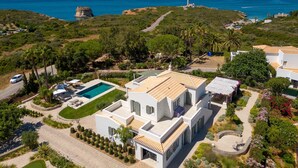 Una propiedad costera con piscina, un faro al fondo y un jardín cuidado.