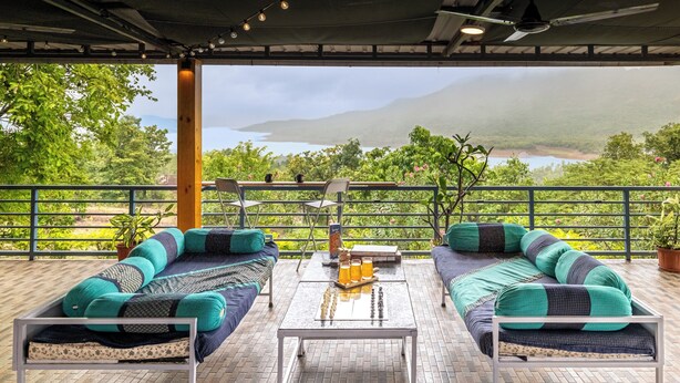 Un espace extérieur aménagé, abrité et doté de deux canapés, d’une table et offrant une vue sur un lac et des montagnes.