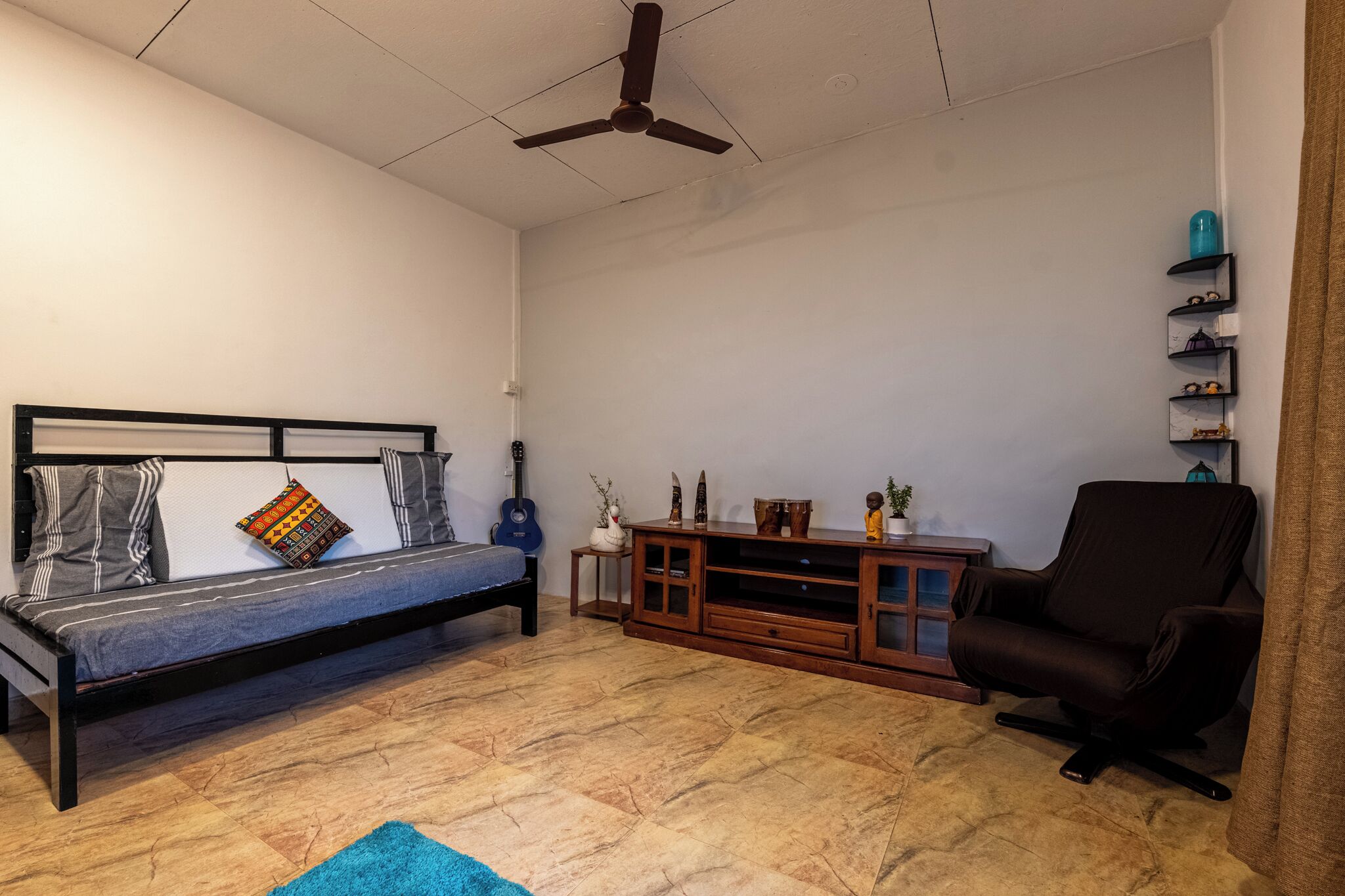 Ein Schlafzimmer mit Bett, Schreibtisch, Stuhl, Deckenventilator und einem kleinen Regal mit Dekoration.
