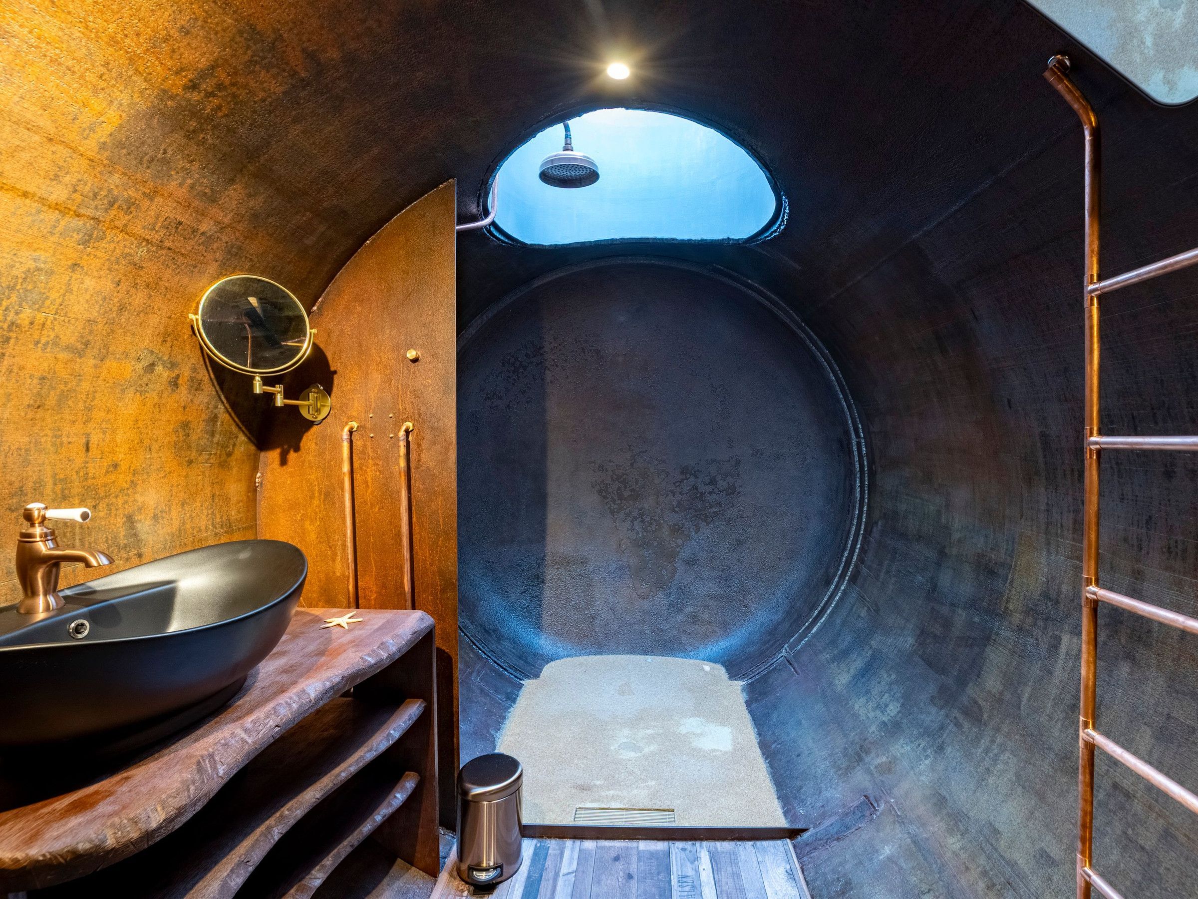 Une petite pièce de forme circulaire, avec un lavabo rond, un petit miroir et un porte-serviettes.
