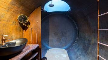 Une petite pièce de forme circulaire, avec un lavabo rond, un petit miroir et un porte-serviettes.