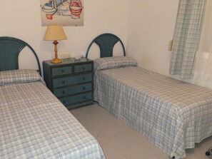 A bedroom with two single beds, a nightstand with a lamp, and a painting on the wall. - Apartment with port view, pets allowed - 4 guests (Roses)