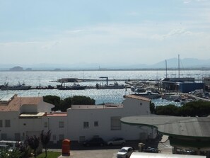 A marina with boats docked, a building with a flat roof, and a clear view of the water and distant mountains. - Apartment with port view, pets allowed - 4 guests (Roses)