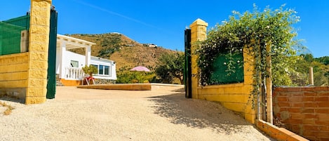 A gated entrance to a property with a white building, a green roof, and a clear blue sky.
