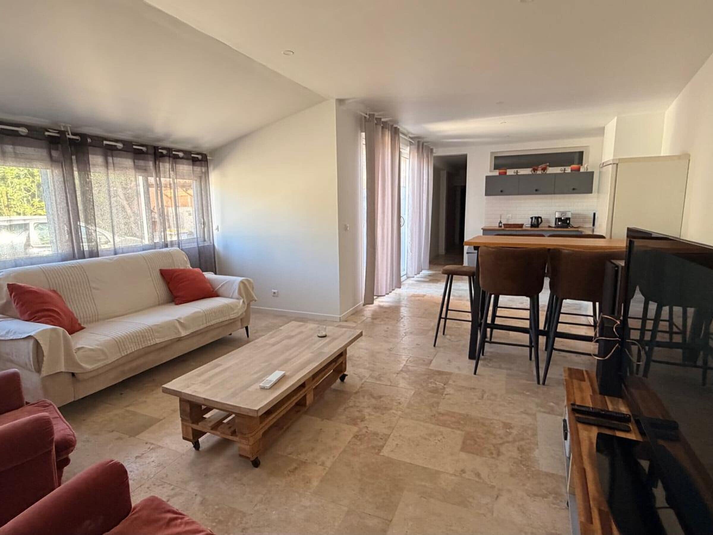 A living room with a sofa, coffee table, and a dining area with chairs and a kitchen in the background.