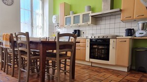 A kitchen with a dining table, chairs, a clock, cabinets, and a stove. - Welcoming gîte near Verdun - 7 guests (Brainville)