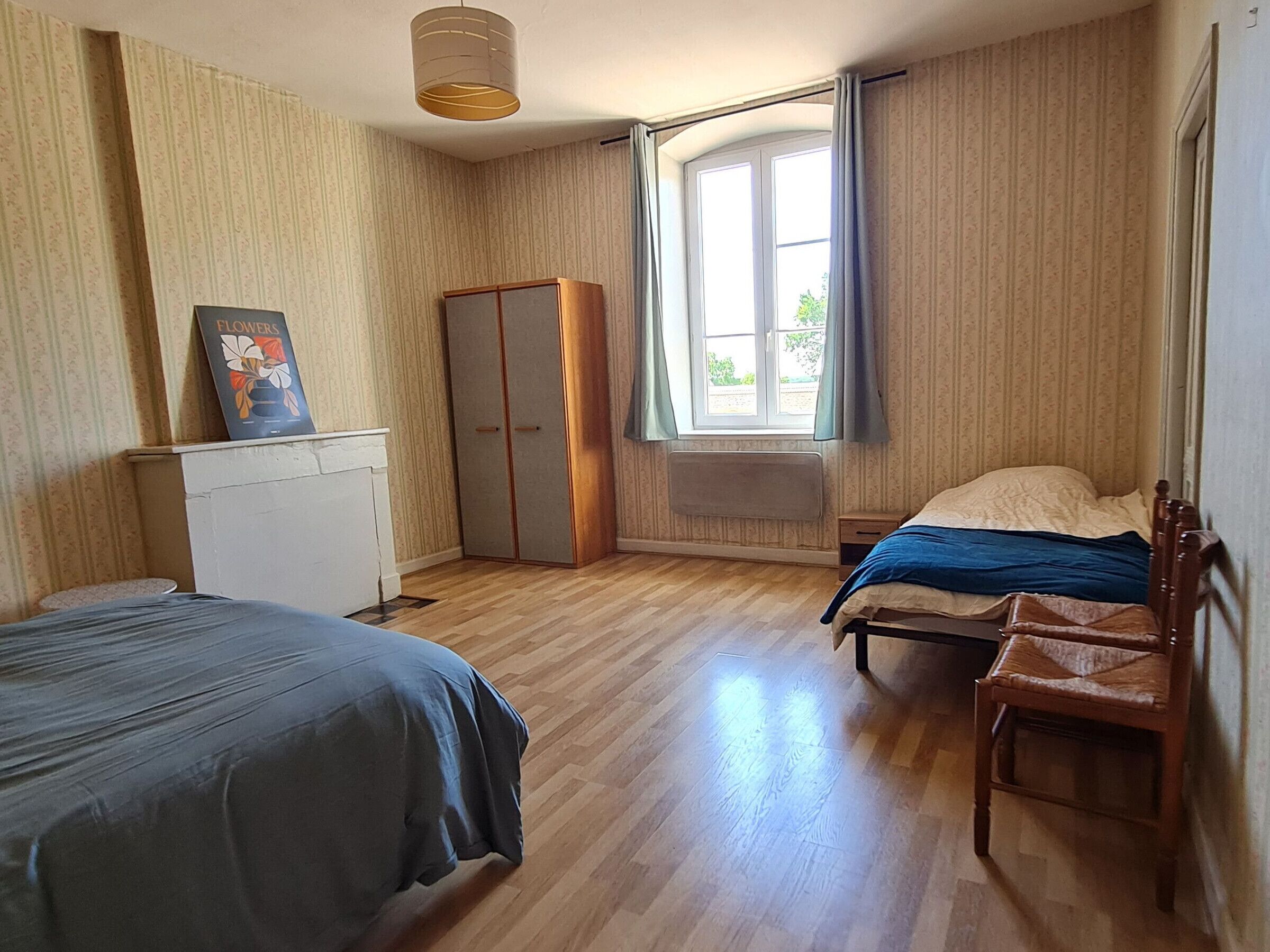 A bedroom with two beds, a wardrobe, a radiator, and a window with curtains.