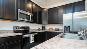 A modern kitchen with dark cabinetry, stainless steel appliances, granite countertops, and a double sink. - Bright 4BR w PS4 Mickey Rooms at Holly Village 132 (Davenport)