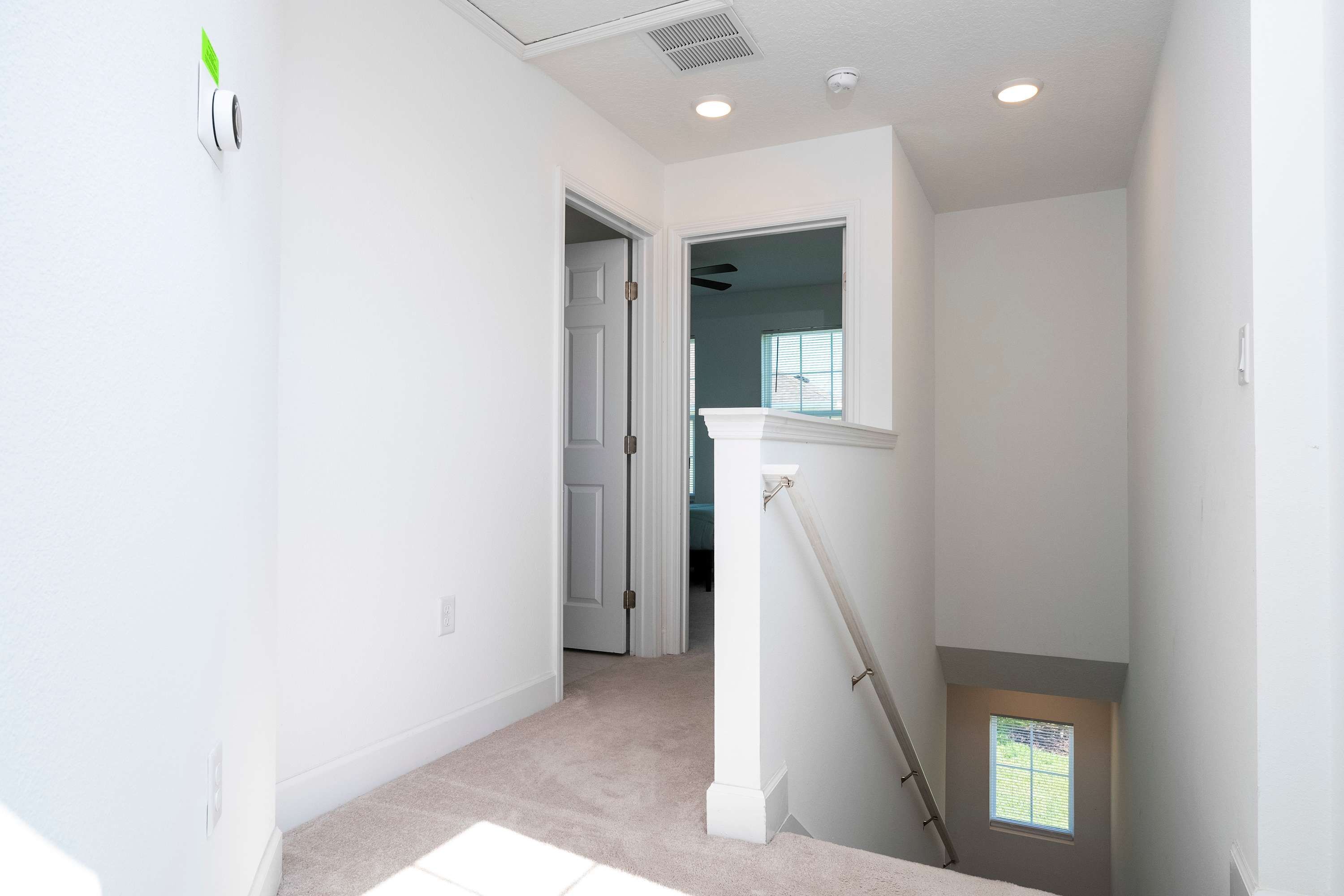 A clean, white hallway with a carpeted floor, a door leading to another room, and a window with blinds.