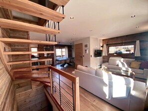 Un interno moderno con una scala in legno, una zona living con divano e TV, e un'area pranzo.