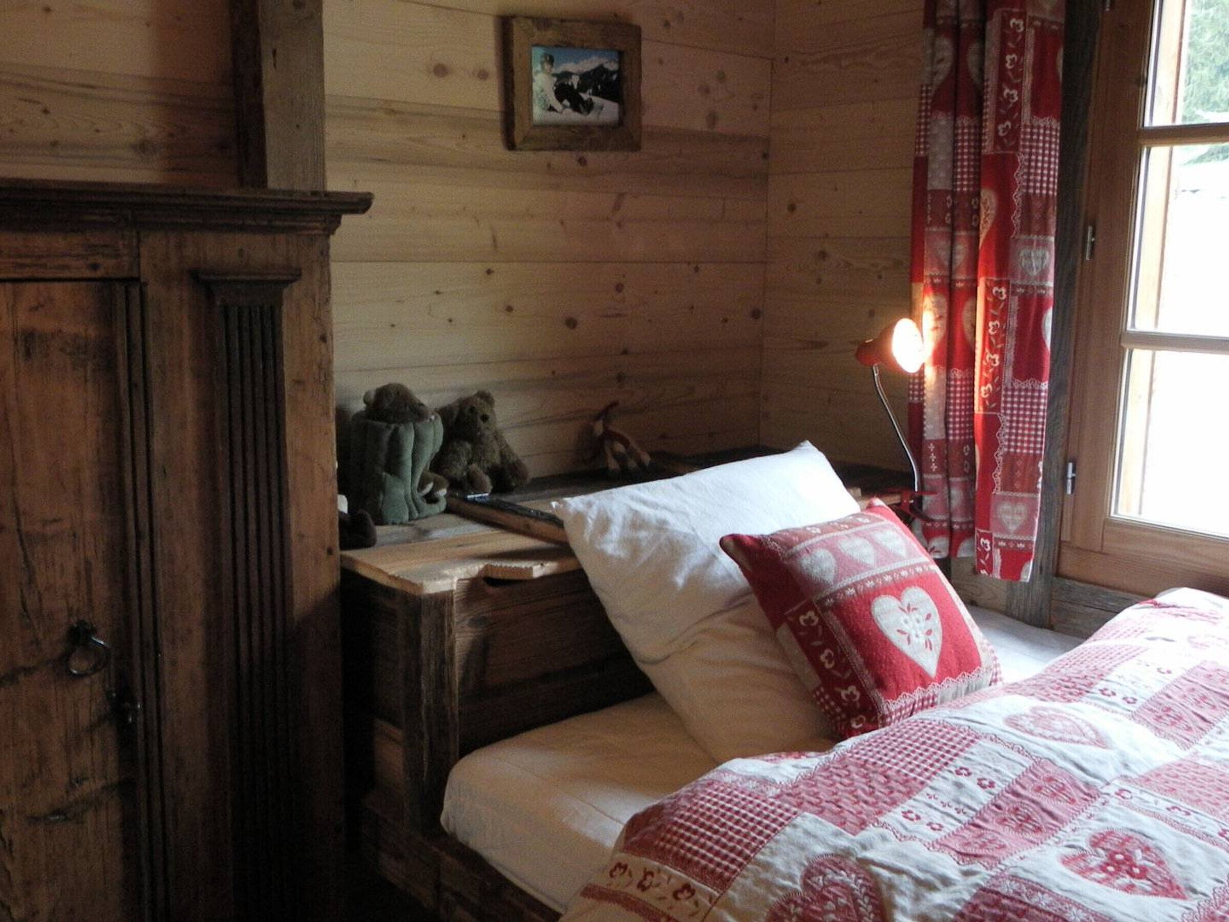 Une chambre dans une cabane en bois, avec un lit, une commode et une fenêtre avec des rideaux.
