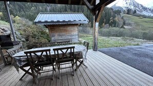 En träaltan med ett bord och stolar, en grill och utsikt över ett bergigt landskap.