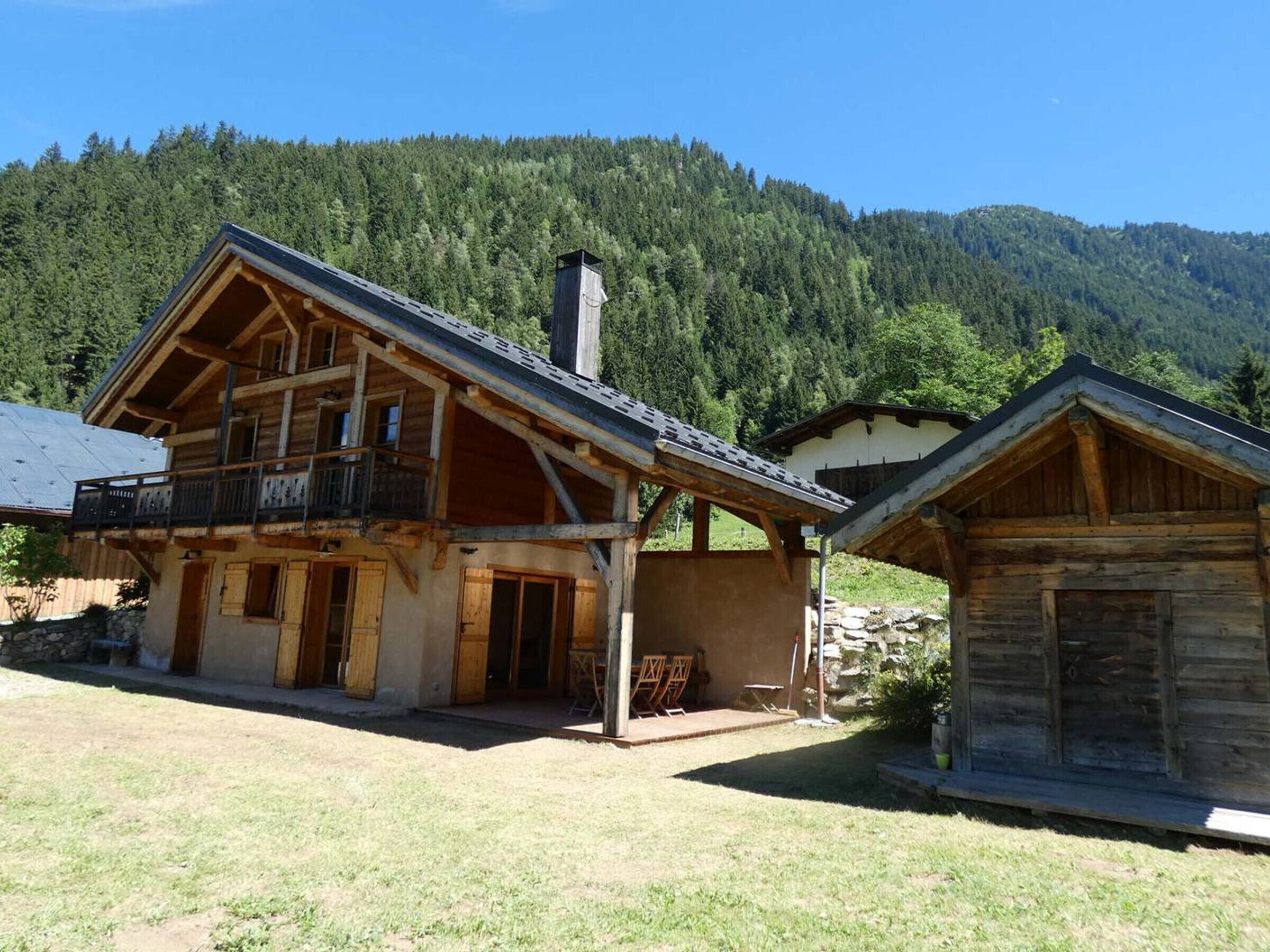A wooden chalet with a balcony, a chimney, and a mountain backdrop.