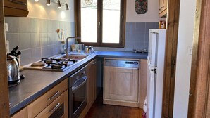 A compact kitchen with a gas stove, oven, dishwasher, and wooden cabinets. - Cozy chalet, pets welcome, mountain view - 11 guests (Beaufort)