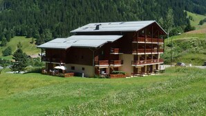 A two-story wooden chalet with balconies, set in a mountainous area with a forest backdrop. - Studio at the foot of the slopes - 5 guests (Arêches-Beaufort)