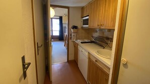 A narrow kitchen with wooden cabinets, a microwave, and a sink. - Studio at the foot of the slopes - 5 guests (Arêches-Beaufort)