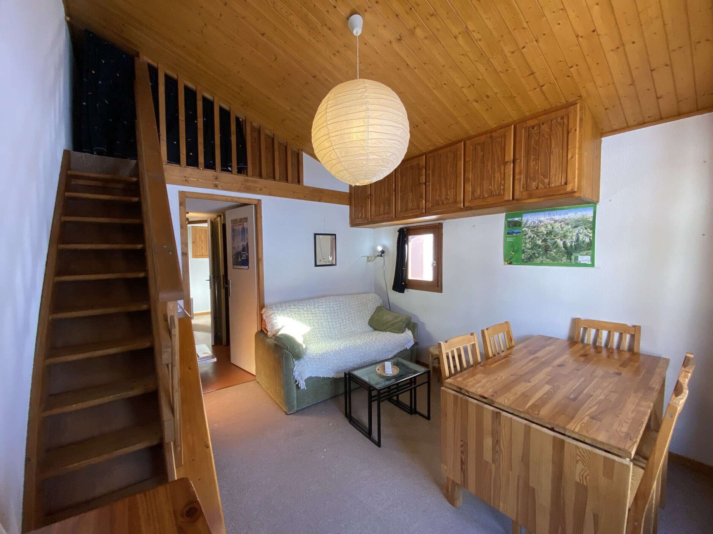 A wooden interior with a bed, a dining table, and a staircase.