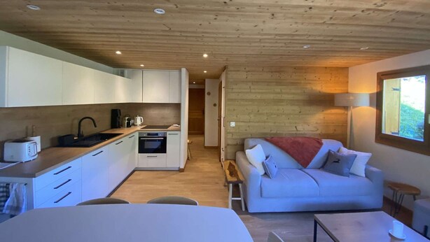 Una cocina compacta con electrodomésticos modernos, un comedor con mesa y sillas, y una sala de estar acogedora con sofá y ventana.