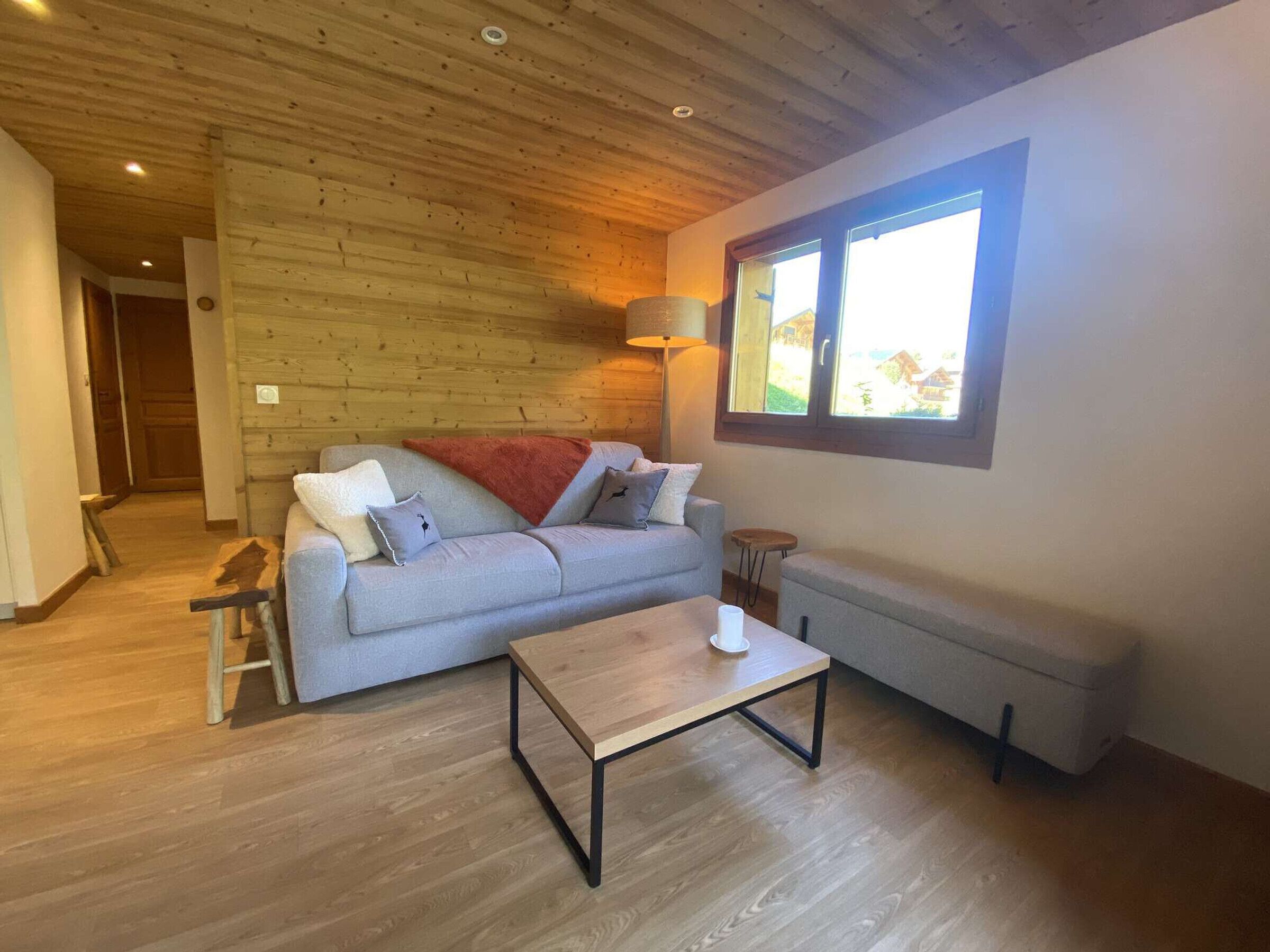 Un accogliente soggiorno con soffitto in legno, un divano grigio, un tavolino e una finestra con vista.