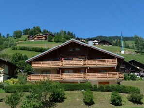 Ein mehrstöckiges Gebäude mit Balkon, umgeben von Grünflächen und weiteren Gebäuden in einer hügeligen Landschaft.
