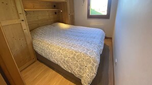 Una habitación pequeña y acogedora con cama, paredes de madera, una ventana y una puerta.