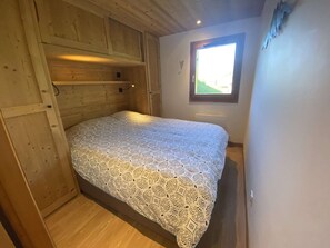 Ein kleiner, gemütlicher Raum mit einem Bett, Holzwänden, einem Fenster und einer Tür.
