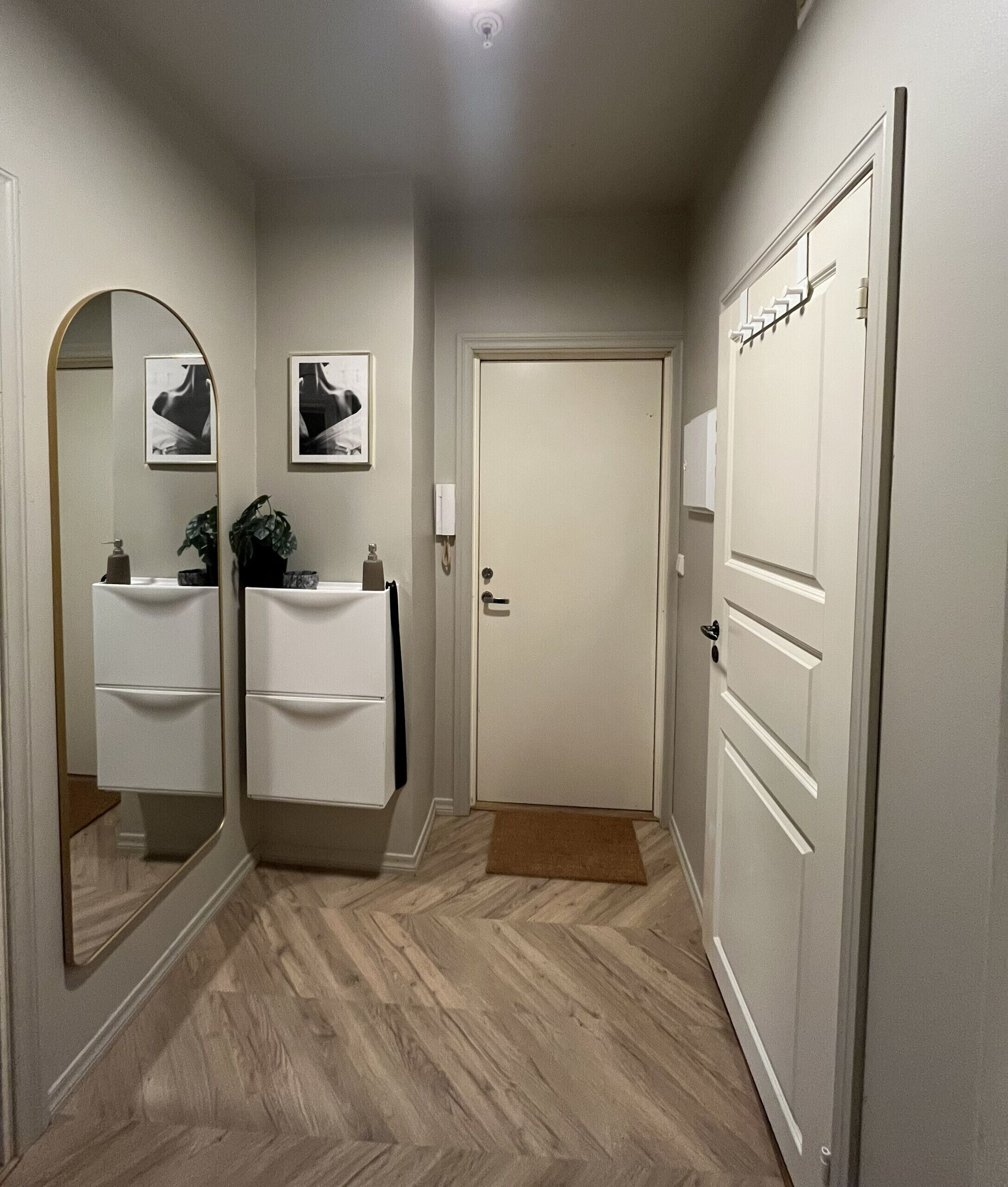 A hallway with a mirror, two sinks, a door, and a small rug.