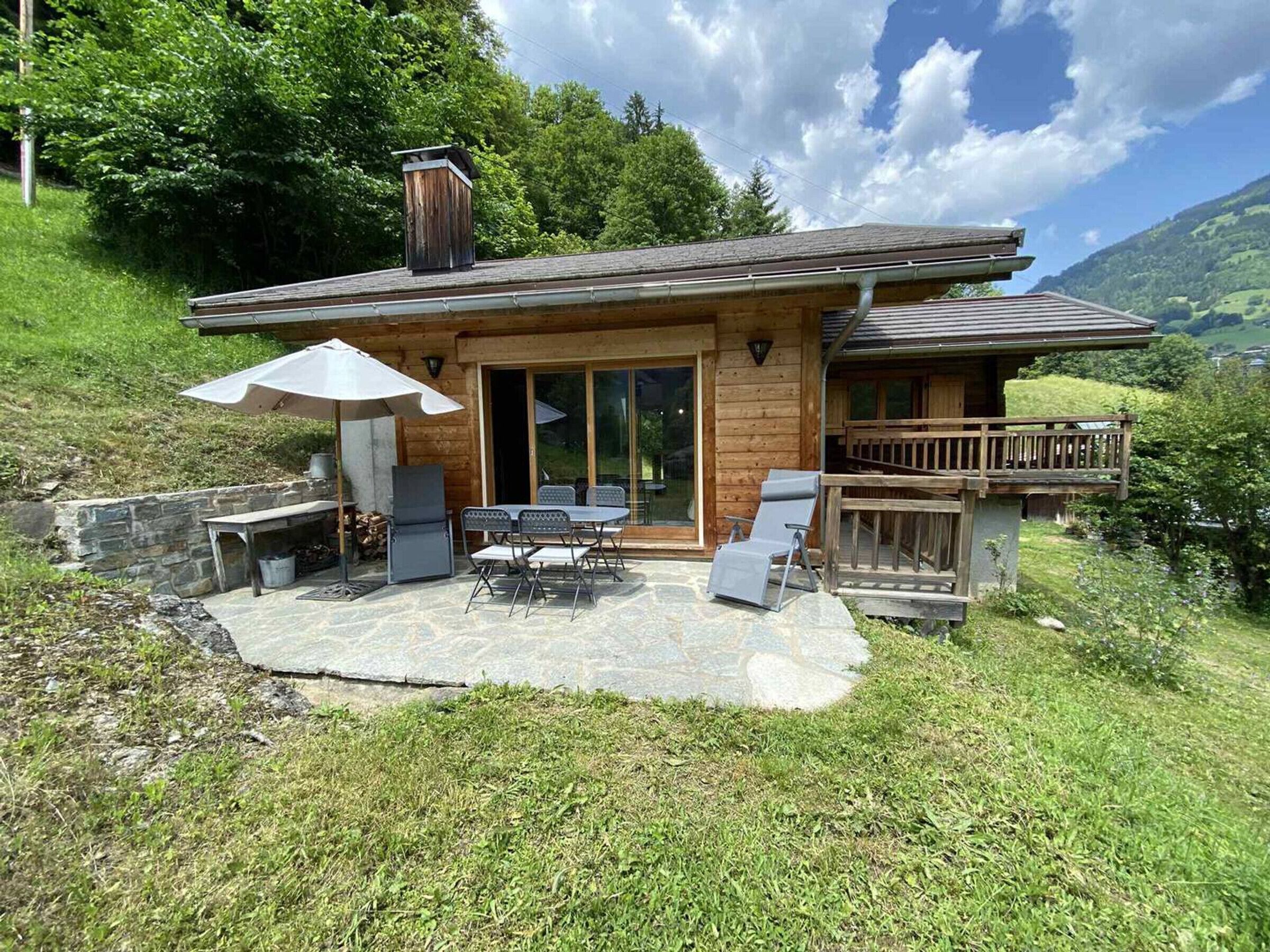 Een houten chalet met terras, buitenmeubels en een veranda met uitzicht op een vallei.